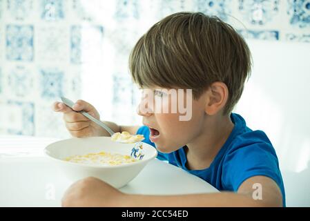 Un garçon dans un T-shirt bleu a le petit déjeuner avec des flocons d'avoine et du lait dans une assiette blanche, espace pour le texte, isoler Banque D'Images