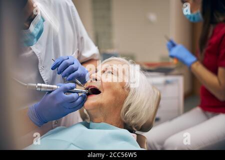 Homme dentiste avec outils dentaires et perceuse tout en prenant soin du patient dents au bureau de la clinique dentaire Banque D'Images