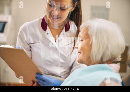 Patient souriant de la clinique dentaire regardant le presse-papiers Banque D'Images