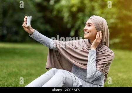 Belle fille dans hijab prenant selfie sur smartphone Banque D'Images