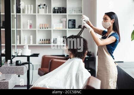 Jeune fille noire dans le masque de protection du visage obtenir la coupe de cheveux à coiffeurs Banque D'Images