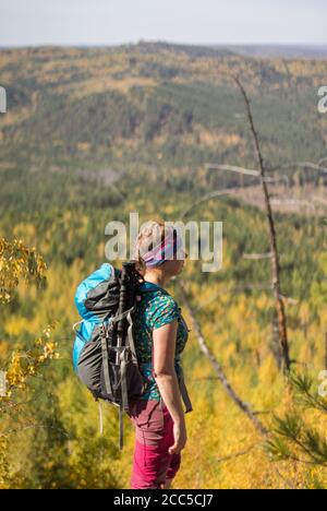 Fille aux cheveux rouges debout avec un sac à dos sur un rocher un fond de forêt d'automne Banque D'Images