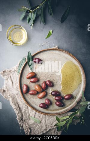 Olives noires et huile d'olive dans l'assiette sur fond gris foncé, vue du dessus Banque D'Images