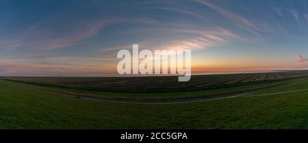 Coucher de soleil panoramique avec de doux nuages colorés sur une pelouse très verte et la mer Banque D'Images