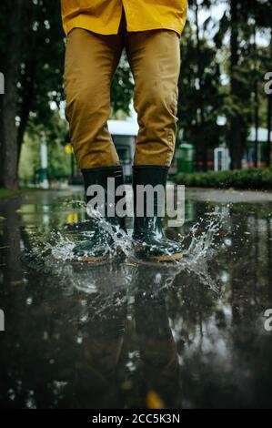 Homme dans des bottes en caoutchouc sautant dans des flaques Banque D'Images