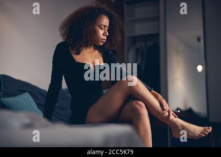 Femme fatiguée pieds nus assise à pieds croisés sur le canapé Banque D'Images