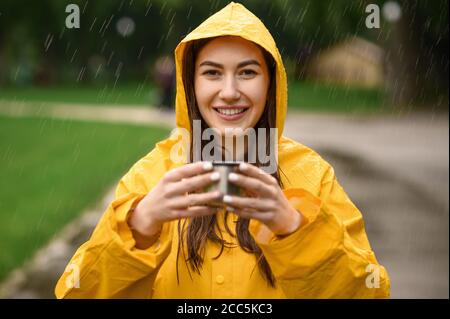 Femme en imperméable tient une tasse, vue à travers les gouttes Banque D'Images