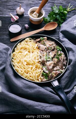 sauce aux champignons à la crème aigre, servi avec des nouilles aux œufs dans une poêle sur une table en bois sombre, vue verticale depuis le dessus Banque D'Images