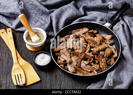 steak de bœuf ribeye frit tendre et juteux coupé en lanières, steak minute, sur une poêle sur une table en bois sombre, vue sur le paysage depuis le dessus Banque D'Images