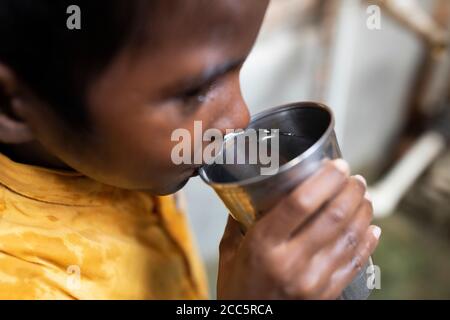 Un garçon de huit ans boit de l’eau tirée du nouveau robinet que sa mère avait récemment installé dans la maison de la famille à Bihar, en Inde. Banque D'Images