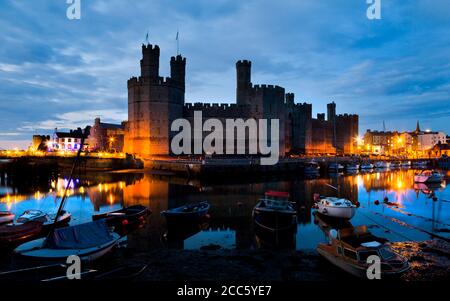 Château de Caernarfon tourné de nuit avec la rivière et les bateaux, au nord du pays de Galles Banque D'Images