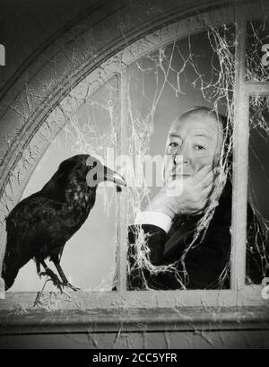 Le réalisateur Alfred Hitchcock, qui fait un pas dans une fenêtre couverte de toiles d'araignée, à côté d'un corbeau dans une photo de publicité pour l'émission télévisée, « The Alfred Hitchcock Hour » vers 1965 CBS File Reference # 34000-267THA Banque D'Images