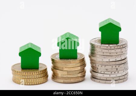 Trois piles de pièces en euros avec des maisons en forme de flèche verte sur fond blanc Banque D'Images