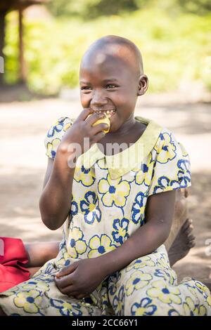 Une jeune fille de neuf ans originaire du Soudan du Sud mange un repas de patates douces à l'extérieur de sa maison, dans le camp de réfugiés de Palabek, dans le nord de l'Ouganda, en Afrique de l'est. Banque D'Images