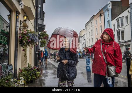 Tenby, pays de Galles de l'Ouest. 19 août 2020. Météo au Royaume-Uni : deux femmes ont fait la queue sous la pluie devant un café dans la rue haute à Tenby, Pembrokeshire portant des vêtements sociaux de temps humide. Le pays de Galles de l'Ouest a été frappé pendant la nuit et pendant le jour d'été suivant avec des tempêtes de pluie et de mauvais temps, Royaume-Uni. Mercredi 19 août 2020. Tenby, Pembrokeshire, West Wales, UK Credit: Jeff Gilbert/Alay Live News Banque D'Images