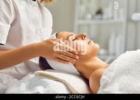 Massage du visage au spa. Une esthéticienne propose un massage du visage à une femme dans un salon de beauté blanc Banque D'Images
