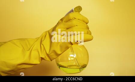 Main dans le gant en caoutchouc jaune contenant le flacon pulvérisateur en plastique avec détergent de nettoyage sur fond jaune Banque D'Images