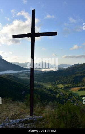 Croix chrétienne sur une montagne, tôt le matin, ciel bleu, brouillard dans la vallée, montagnes en arrière-plan, la Beaume, Hautes Alpes, France Banque D'Images