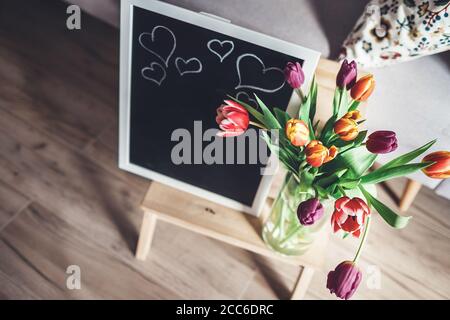 Des tulipes colorées dans un vase avec un tableau de chalk sont au sol dans la salle de séjour Banque D'Images