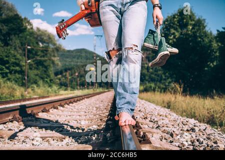 Jeune homme avec la guitare marche sur la voie ferrée, gros plan jambes image Banque D'Images