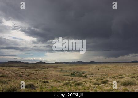 Paysage désertique et spectaculaire avec des prairies arides, des montagnes lointaines et des nuages de pluie sombres et orageux Banque D'Images