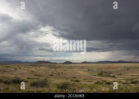 Paysage désertique et spectaculaire avec des prairies arides, des montagnes lointaines et des nuages de pluie sombres et orageux Banque D'Images