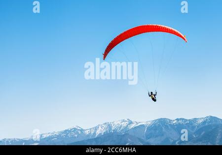 Un sportif sur un parapente rouge qui survole les sommets enneigés des montagnes Banque D'Images