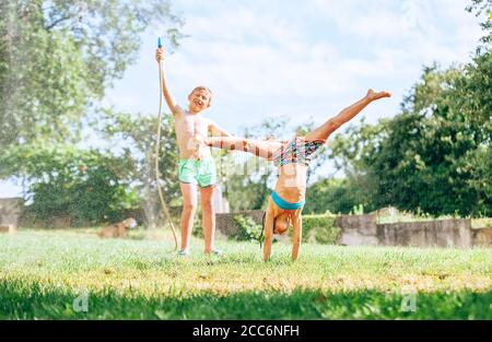 Les enfants heureux se métrompent dans le jardin d'été, éclaboussant l'eau et sautant Banque D'Images