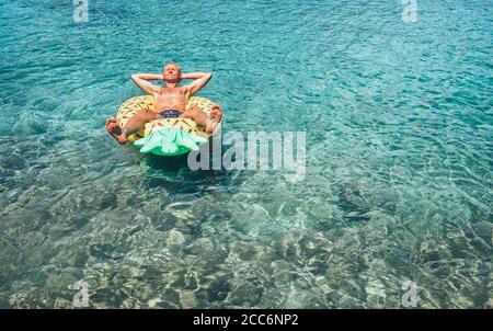 L'homme a le temps de se détendre lorsqu'il naque dans la piscine d'ananas gonflable anneau dans l'eau de mer cristalline Banque D'Images
