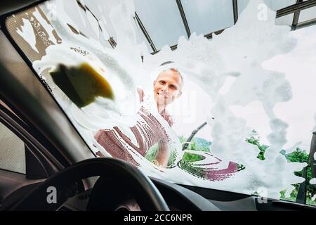 Homme lave les vitres avant de voiture avec de la mousse de savon Banque D'Images