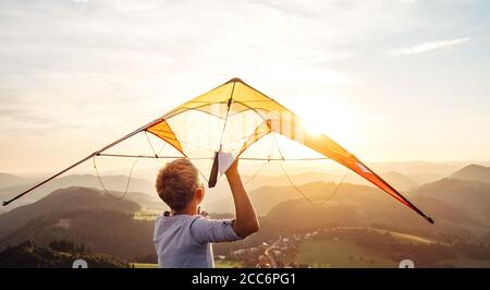 Garçon commence à voler un cerf-volant sur les collines de montagne au coucher du soleil Banque D'Images