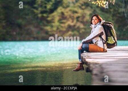 Calme femme souriante voyageur assis sur le pont en bois près de la lac de montagne le jour d'automne ensoleillé Banque D'Images