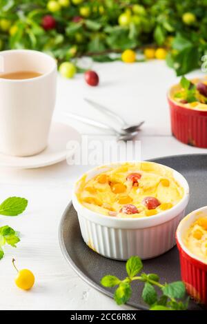 Délicieux clafoutis à base de yaourt blanc et de baies, dessert de prune cerise dans des bols en forme de porc sur la table avec une tasse de jus Banque D'Images