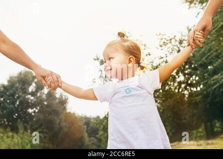 Petite fille de 2 ans marchant avec des parents tenant leur une image d'été éclatante pour les mains Banque D'Images