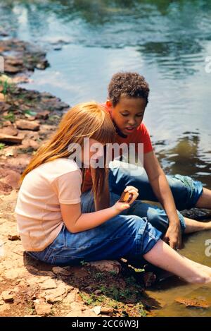 ANNÉES 1970 DEUX ENFANTS PRÉADOLESCENTS FILLE CAUCASIENNE ET GARÇON AFRO-AMÉRICAIN PORTER UN JEAN BLEU ASSIS DANS L'EAU EN COURS D'EAU - 065535 TAY001 HARS AMITIÉ DEMI-LONGUEUR PIERRES RUISSEAU MÂLES DENIM MIXTE PRÉADOLESCENTS GARÇON GRAND ANGLE DÉCOUVERTE AVENTURE AFRO-AMÉRICAINS AFRO-AMÉRICAIN ET LOISIRS REDHEAD NOIR ETHNICITÉ CURLY DANS PIEDS NUS PRETEEN ROCHES ROUGES CHEVEUX DIVERS BLEU JEANS D'ENFANCE JUVÉNILES MIXTE RACE PRÉ-ADOLESCENCE PRÉ-ADOLESCENT PRÉ-ADOLESCENT FILLE TOGETHERNESS RACE BLANCHE INNOCENT OLD FASHIED AFRO-AMÉRICAINS Banque D'Images