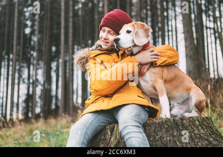 Portrait de deux meilleurs amis qui s'embrasent - garçon et son chien de beagle s'assoient sur la souche de l'arbre dans la forêt d'automne. Banque D'Images