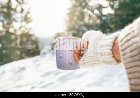 Femme prendre en main une tasse de boisson chaude. Hiver forêt de glades, scène ensoleillée Banque D'Images