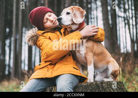 Portrait de deux meilleurs amis qui s'embrasent - garçon et son chien de beagle s'assoient sur la souche de l'arbre dans la forêt de pins d'automne. Banque D'Images