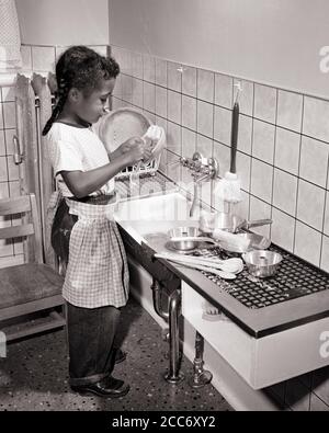 ANNÉES 1950, UNE PETITE FILLE AFRO-AMÉRICAINE LAVANT SON JOUET PLATS POT CASSEROLES DANS UN ÉVIER DE CUISINE DE TAILLE ENFANT À LA GARDERIE LE JOUR DE L'ÉCOLE ENTRETIEN - N561 HAR001 HARS HEALTH COPY SPACE LAVABO PLEINE LONGUEUR CONFIANCE B&W PAN DES OBJECTIFS PLUS CORPULENT LES CONNAISSANCES AFRO-AMÉRICAINES AFRO-AMÉRICAINES D'ORIGINE ETHNIQUE NOIRE FIERTÉ OPPORTUNITÉ CONNEXION ANONYME COOPÉRATION CROISSANCE MINEURS TÂCHE NOIRE ET BLANC HAR001 AFRO-AMÉRICAINS À L'ANCIENNE Banque D'Images