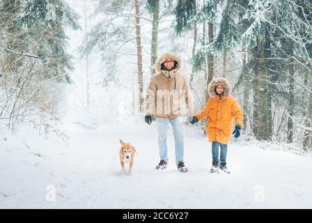 Père et fils vêtus de chaud capuche décontracté Parka Veste Outerwear marchant dans la forêt enneigée avec son chien de beagle dans la forêt de pins. Famille marchant avec pe Banque D'Images