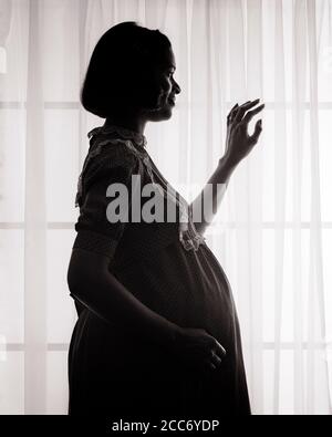 FEMME ENCEINTE AFRO-AMÉRICAINE DES ANNÉES 1970 SILHOUETÉE DEVANT LA FENÊTRE AVEC VOILES RIDEAUX - S20967 HAR001 HARS JOIE VIE SATISFACTION PARENT CÉLÉBRATION FEMMES STUDIO PRISE DE VUE SANTÉ MAISON VIE COPIE ESPACE DEMI-LONGUEUR FEMMES PERSONNES INSPIRATION SÉRÉNITÉ SPIRITUALITÉ CONFIANCE B&W TRISTESSE PERSONNES ENCEINTES HISTOIRE DE RÊVES MATERNELS BONHEUR BIEN-ÊTRE SILHOUETTED AFRO-AMÉRICAINS AFRO-AMÉRICAIN EXPECTANT EXPECTANT MÈRE NOIR ETHNIE MATERNITÉ FIERTÉ CONCEPTUELLE MATERNITÉ EN FACE DE EN ATTENTE DE CROISSANCE ADULTE MOYEN-ADULTE FEMME MOYENNE-ADULTE MAMAN JEUNE ADULTE FEMME NOIRE ET BLANC HAR001 À L'ANCIENNE Banque D'Images