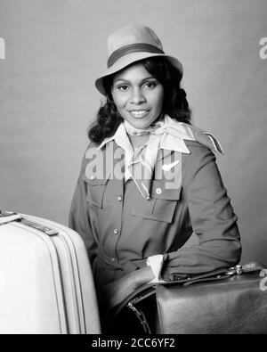 LES ANNÉES 1970, UNE FEMME AFRO-AMÉRICAINE SOURIANTE, HÔTESSE DE LA COMPAGNIE AÉRIENNE, A POSÉ AVEC SON SAC À MAIN PORTER UN CHAPEAU REGARDANT LA CAMÉRA - S20923 HAR001 CARRIÈRE HARS JEUNE ADULTE SÉCURITÉ HEUREUX JOIE STYLE DE VIE COMPAGNIE AÉRIENNE FEMMES EMPLOIS SANTÉ ESPACE DE COPIE DEMI-LONGUEUR FEMMES PERSONNES PROFESSION CONFIANCE TRANSPORT EXPRESSIONS B&W. CONTACT VISUEL COMPÉTENCE PROFESSION BONHEUR COMPÉTENCES BIEN-ÊTRE ENJOUÉ AVENTURE FORCE SERVICE À LA CLIENTÈLE AFRO-AMÉRICAINS AFRO-AMÉRICAINS CARRIÈRES SAVOIR RACE NOIRE FIERTÉ AUTORITÉ OCCUPATIONS SOURIRES CONCEPTUEL JOYEUX ÉLÉGANT ASSISTANT DE VOL COMPÉTENT POSA L'HÔTESSE JEUNE FEMME ADULTE Banque D'Images