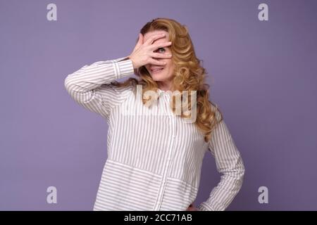 Femme caucasienne couvrant le visage et piquant à travers les doigts, regardant la caméra Banque D'Images