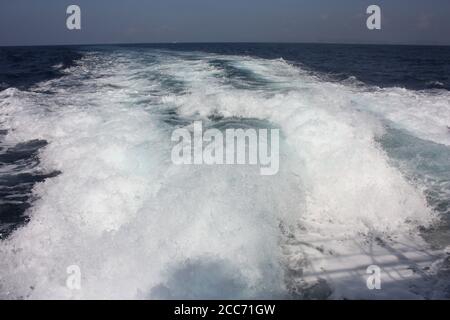 sentier en mousse blanche laissé dans les vagues bleues de l'océan par un bateau et le ciel Banque D'Images