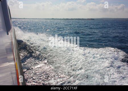 sentier en mousse blanche laissé dans les vagues bleues de l'océan par un bateau et le ciel Banque D'Images