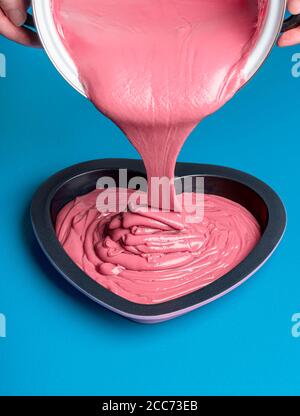 Le chocolat rubis fondu verse dans un moule en forme de coeur sur fond bleu. Nouvelle catégorie de chocolat. Goutte de glaçage rose. Dessert belge. Banque D'Images