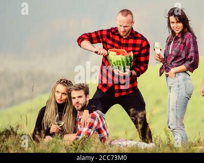 Séjour sans soucis entre amis. Randonnée. Amis heureux, hommes et filles, mangent de la pastèque. Pique-nique romantique dans le camp de tourisme. Vacances d'été. Groupe de personnes passent du temps libre ensemble. Camping familial. Banque D'Images