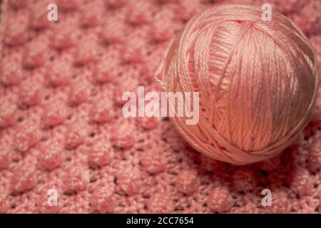 Boule de fil rose avec fond rose texturé composé de couverture de bébé crochetée en fil rose dans le point de galet également connu comme le point d'ananas Banque D'Images