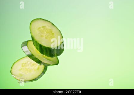 Morceaux de concombre en chute libre avec des gouttes d'huile sur fond vert avec un dégradé Banque D'Images