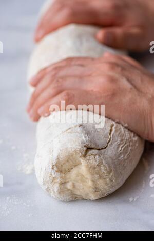 Femme roulant de la pâte à pain dans une bûche sur une surface en marbre. Banque D'Images